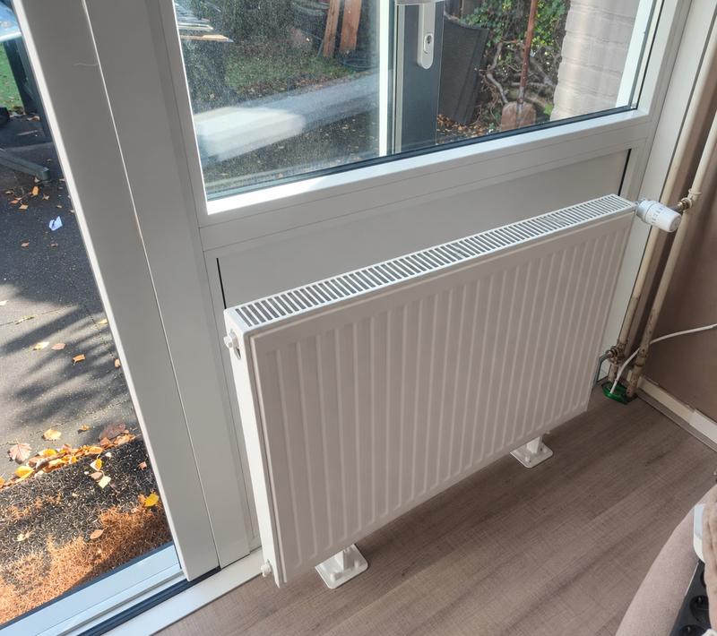 Nieuw geplaatste witte paneelradiator met thermostaatkraan onder een raam